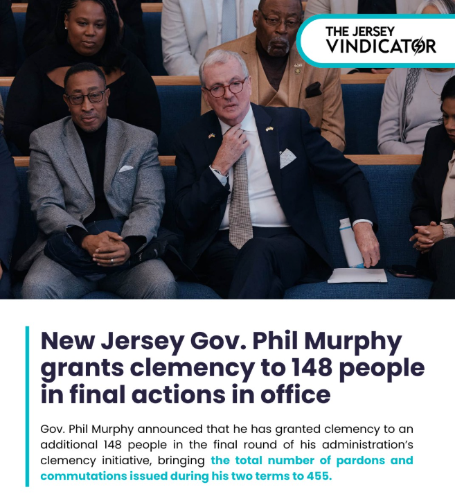 Gov. Phil Murphy sits on a bench in a suit, gesturing while surrounded by others, as an announcement displays that he has granted clemency to 148 people in his final actions as New Jersey governor.